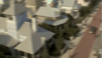 Artistic depiction of a suburban town viewed from above, with a pair of large, realistic blue eyes superimposed in the sky.